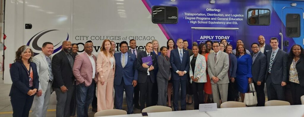 U.S. Deputy Commerce Secretary Don Graves stands with leaders from City Colleges, United Airlines, and P33. They are in front of a bus that reads City Colleges of Chicago Apply Today. Offering: Transportation, Distribution and Logistics, Degree Programs and General Education, High School Equivalency and ESL